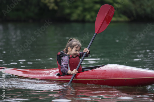 young teenager girl actively manages a sports kayak boat on a beautiful river.