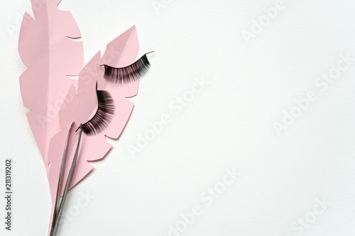 Black false lashes strips with tweezers on pink paper leaves and white background photo