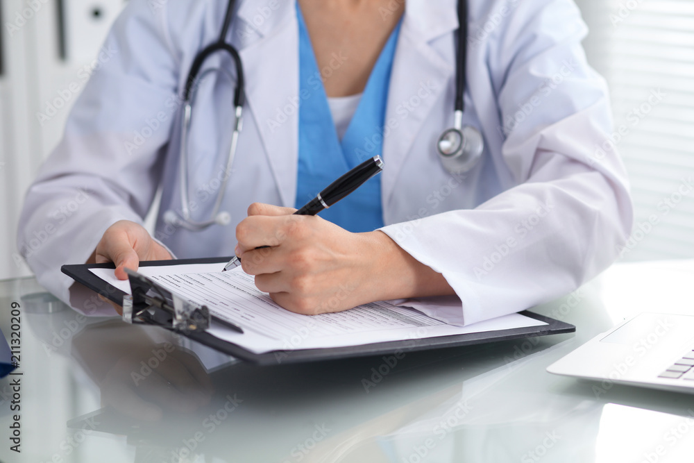 Doctor woman filling up medical form while sitting at the table, close-up of hands Doctor woman filling up medical form while sitting at the table, close-up of hands