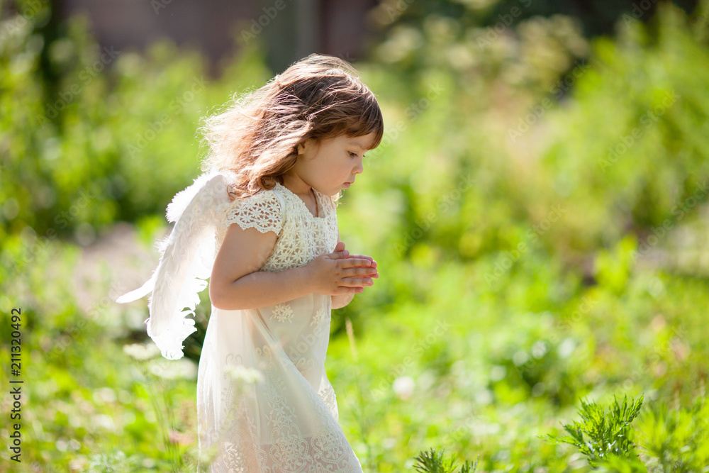 Beautiful little Angel girl standing at the forest with arms close to her chest as in prayer Beautiful little Angel girl standing at the forest with arms close to her chest as in prayer