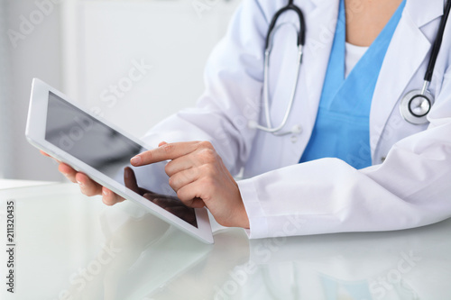 Female doctor using tablet computer while sitting at the workplace, close-up of hands. Medicine, healthcare and help concept