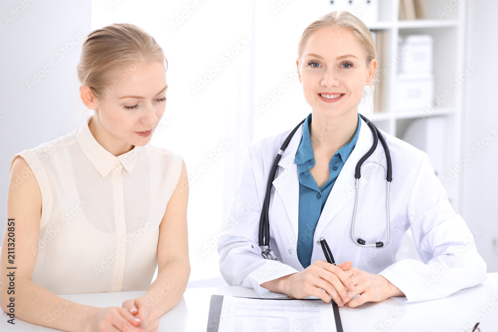 Blonde female doctor and patient talking in hospital office. Health care and client service in medicine Blonde female doctor and patient talking in hospital office. Health care and client service in medicine