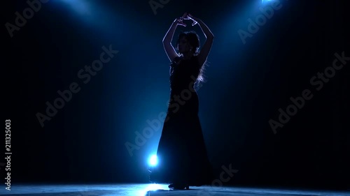 Dancer performs professional flamenco movements. Llight from behind. Smoke background. Silhouette