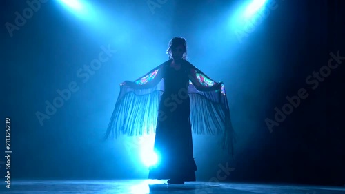 Flamenco. Woman is dancing with a manton in her hands. Llight from behind. Smoke background. Silhouette
