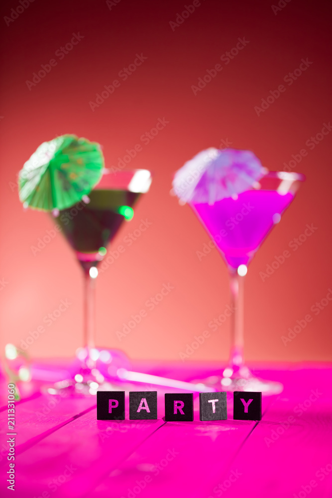 Party invitation image with selective focus on the word party in front of colourful cocktail drinks.