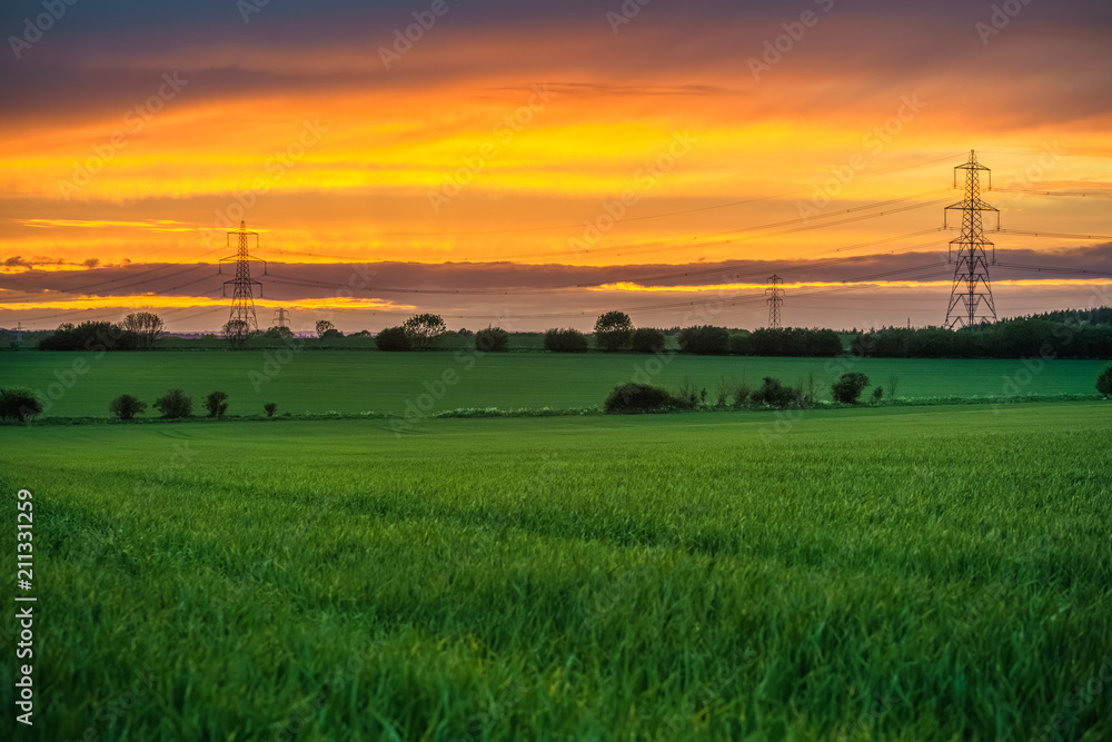 Electric towers and green meadow at sunset Electric towers and green meadow at sunset