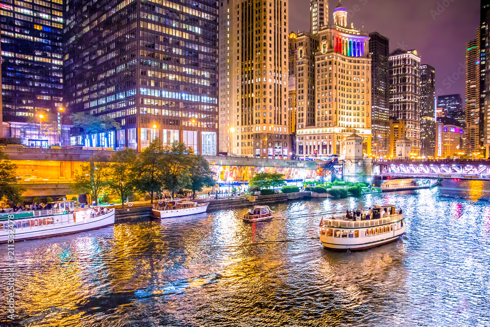 Fototapeta premium Piękne centrum Chicago w nocy z oświetlonymi budynkami, rzeką i mostem.