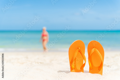 happy beautiful young woman in pink bikini with flip flop on sandy beach, green sea and blue sky background for summer holiday and vacation concept.