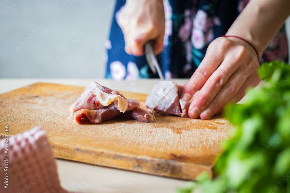 Woman hands cuts raw red meat into pieces with sharp knife on wooden board.