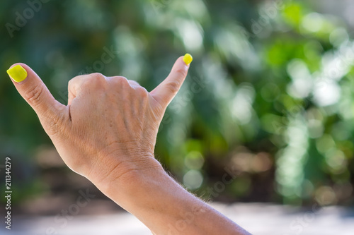 Woman makes hang loose sign in natural light outdoors with room for text © Tim