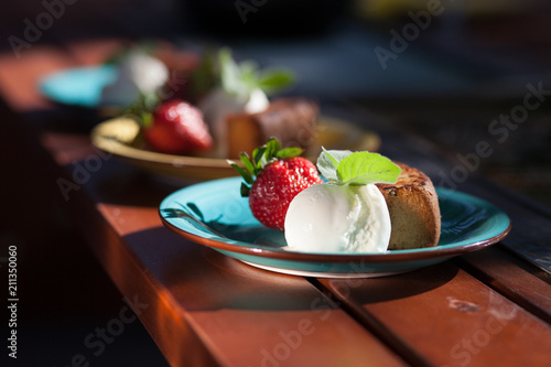 Strawberries with ice cream and biscuits on a blue plate standing on a wooden table