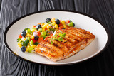 Freshly cooked grilled salmon filet with pepper, corn, blueberry and onion salad close-up on a plate on a table. horizontal