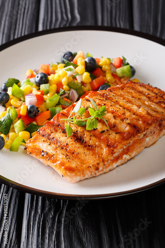 Grilled salmon served with salad salsa of vegetables and berries close-up on a plate. vertical