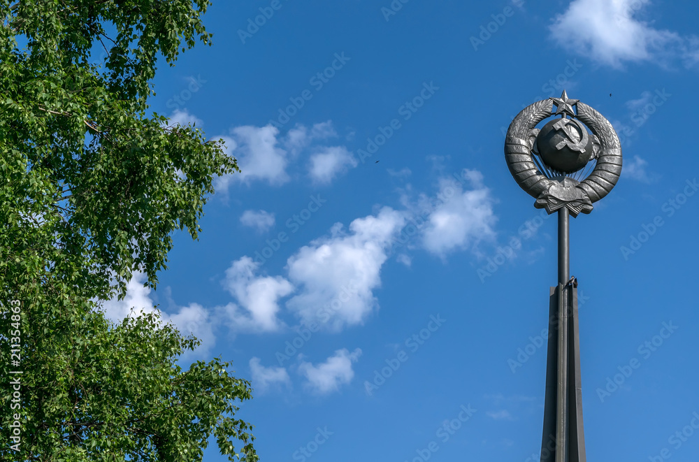 Stella, a monument of the Soviet era hammer and sickle on the background of blue sky and the leaves of the trees
