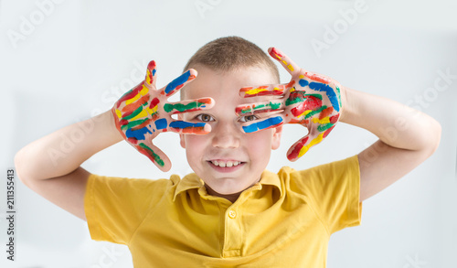 A boy in yellow shirt closed eyes by painted colored hands. Smile hands