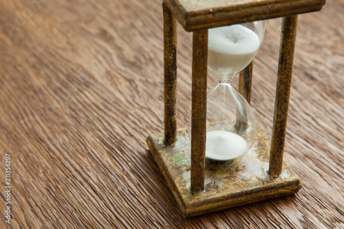 Hourglass on the Oak table as time passing concept for business deadline, urgency and running out of time.