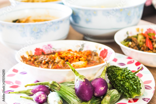 The poor eat a cup of spicy chili paste with vegetables and wild curry on a wooden table.