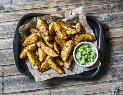 Fototapeta Naklejka Na Ścianę i Meble -  Roasted spices potato with avocado salsa on wooden background, top view. Delicious snack or appetizers. Vegetarian food