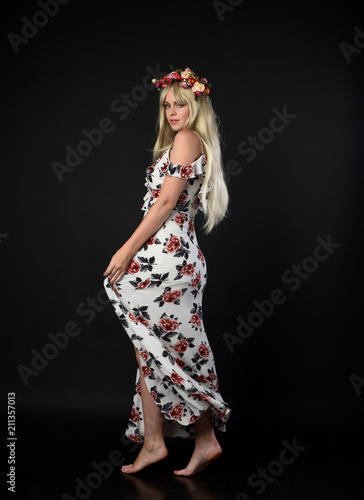 full length portrait of blonde girl wearing floral dress and a flower crown. standing pose against a black studio background. © faestock