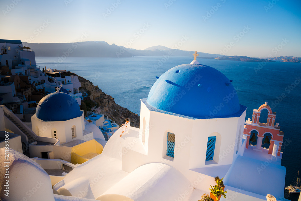 Men in white clothes posing near blue domes on Santorini island, Greece. View on Caldera and Aegean sea from Oia. Active, travel, tourist concepts