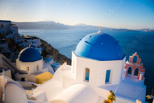 Men in white clothes posing near blue domes on Santorini island, Greece. View on Caldera and Aegean sea from Oia. Active, travel, tourist concepts