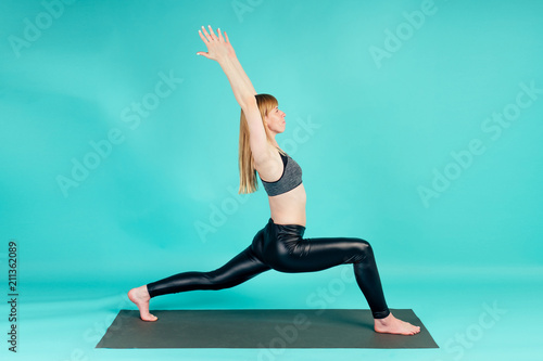 Asanas coach young and active blonde woman practicing yoga and meditating on a yoga mat in studio on blue background
