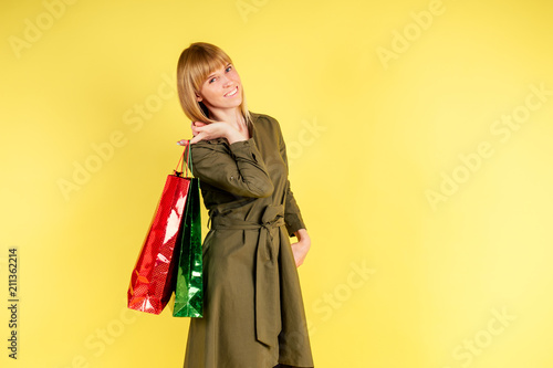young and active blonde woman holds a lot of shopping bags in studio on yellow background . concept of shopaholism and discount
