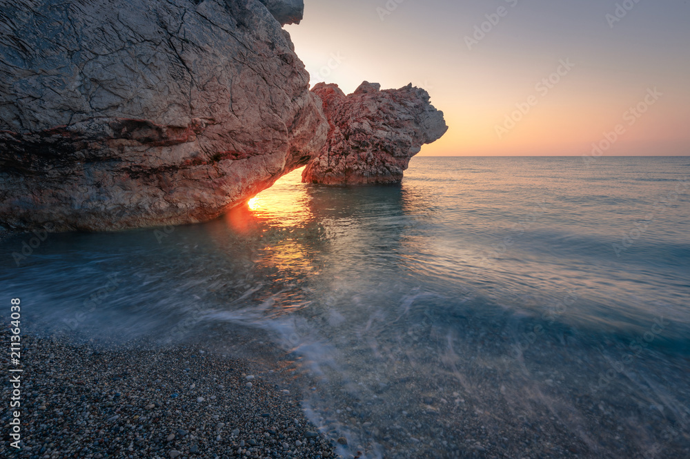 Beautiful sunrise over pebble beach with rocks. Coastal landscape of rocky beach.