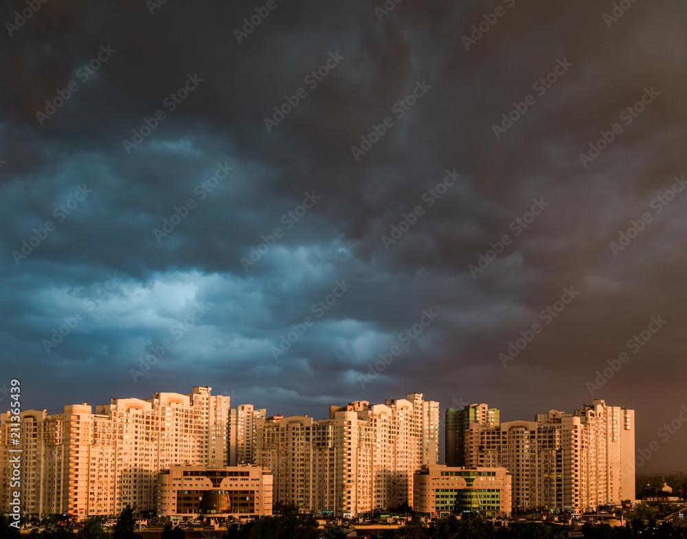 Dramatic stormy clouds over modern residential buildings, in evening sunlight.