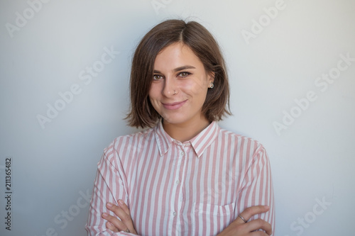 Close up portrait of smiling european woman on gray background. She is crossing hands and looking with confedence at camera