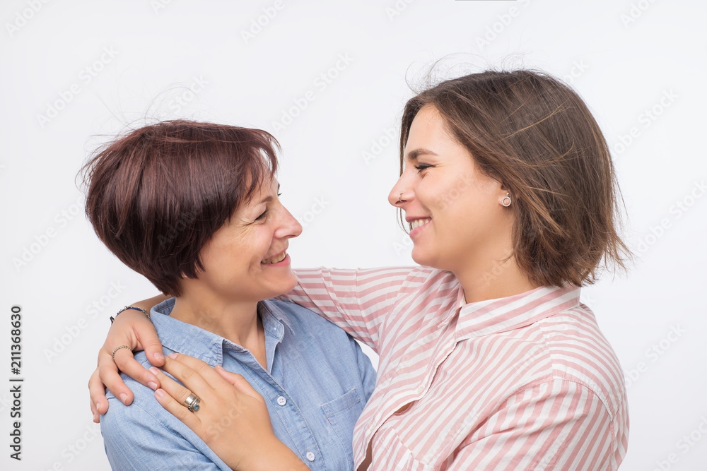 Beautiful maturesenior mom and her adult daughter are hugging, looking at camera and smiling. Good relationships between generations. Beautiful maturesenior mom and her adult daughter are hugging, looking at camera and smiling. Good relationships between generations.