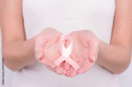 Oncological disease concept. Girl wearing white top holding pink ribbon as a symbol of breast cancer in her hands.