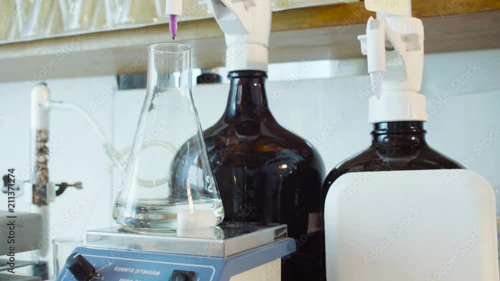 Top view. Chemical analysis laboratory. Close up flask with the test solution on the table of the magnetic stirrer. Scientist titrating solution. Top view. Chemical analysis laboratory. Close up flask with the test solution on the table of the magnetic stirrer. Scientist titrating solution.