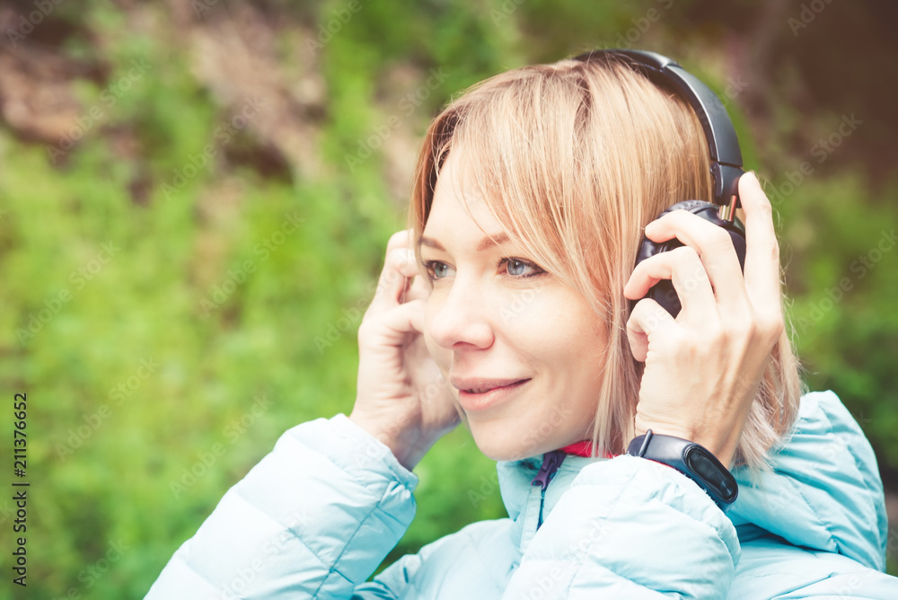 Close up Portrait of a beautiful young woman holding headphones listening to music outdoors in the forest. Joyful music Close up Portrait of a beautiful young woman holding headphones listening to music outdoors in the forest. Joyful music