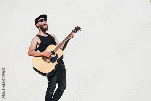 Guitar player singing outside. Hipster guitar player with beard and black clothes photo