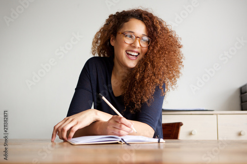 happy female college student sitting at desk writing in book photo