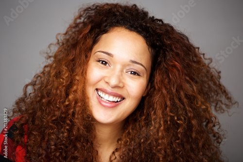 happy young african american woman with curly hair against gray wall