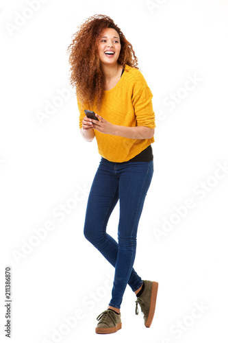Full body happy woman with cellphone laughing against isolated white background