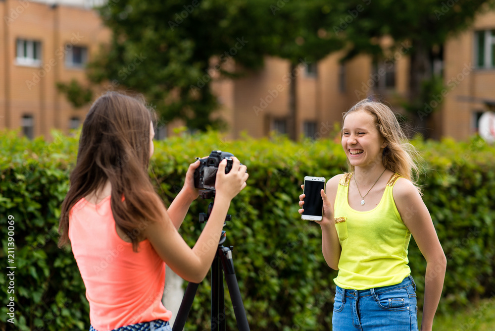 custom made wallpaper toronto digitalTwo girls are teenagers. Summer in nature. Writes the video to the camera. In hands holds the phone. Concept review smartphone. Smiles happily.