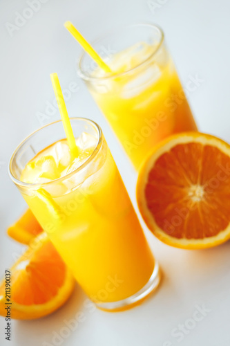 Glasses of fresh orange juice with ice and orange slices on a white background.