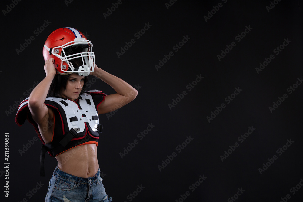 Portrait of sexy attractive young girl with a bright make-up in a sports outfit for rugby with the helmet on head strongly looking forward standing on a black background Portrait of sexy attractive young girl with a bright make-up in a sports outfit for rugby with the helmet on head strongly looking forward standing on a black background