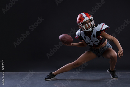 Sexual sportive woman running with rugby ball and screaming aggressively at black background. gender equality