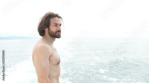 Rear view of young caucasian man with naked torso standing on bow of yacht looking at seascape photo
