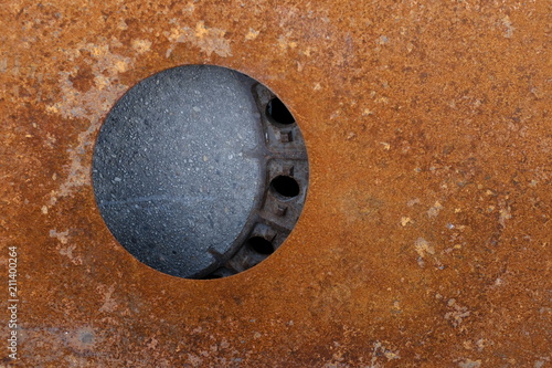 A rusty metal plate with a hole in it. Cover of a gully cover