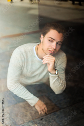 Young man wearing grey sweater sitting, reflection in window. Concept of tourist and resting. photo