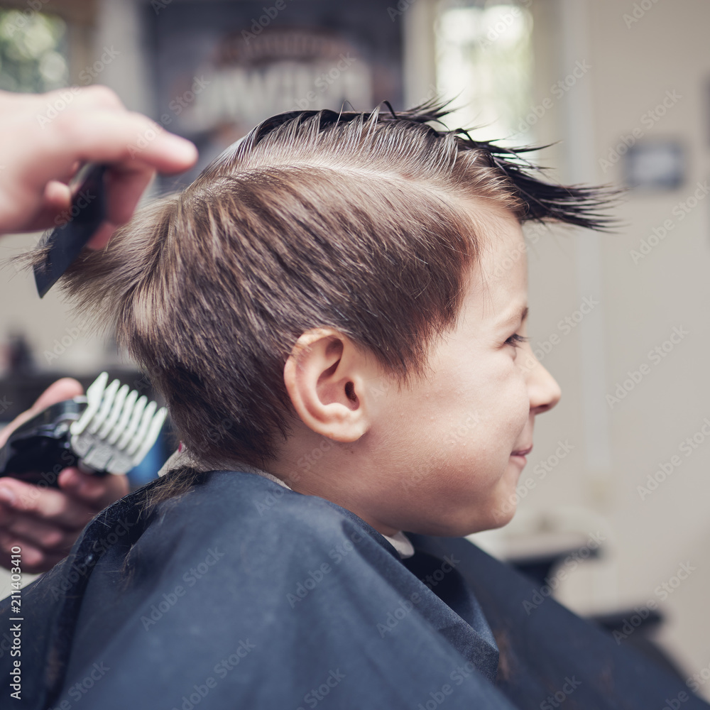 Cheerful Caucasian boy  getting hairstyle in barbershop.