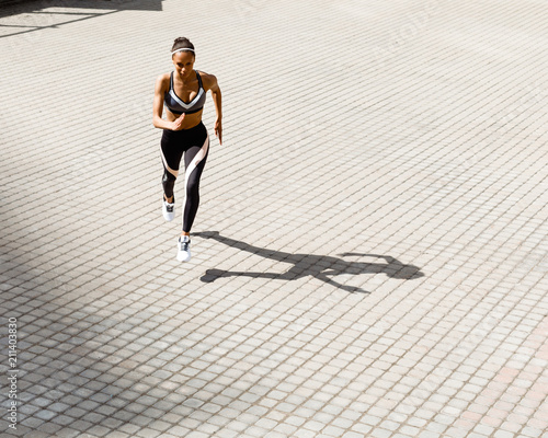 Young muscular woman running on city street, high angle view