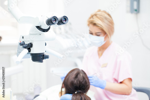 Professional dental endodontic binocular microscope in the treatment room. Against the backdrop of a female dentist and a female patient. Focusing on a microscope