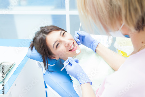 The girl in the medical chair at the dentist  smiling grumbles before the treatment. Woman doctor in mask and gloves medical tools in hands