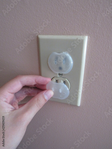 A person inserting a baby proof safety outlet cover into an American outlet